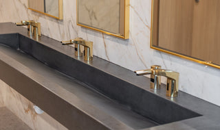 Triple station concrete ramp sink in black with a marble backsplash and gold faucets.