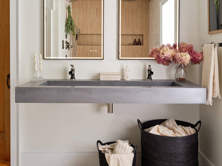 Home bath with double vanity in a smooth concrete with individual mirrors and bronze fixtures.