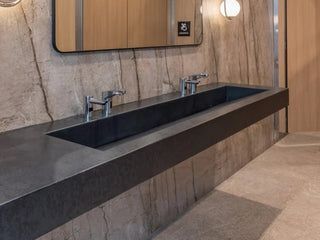 Long, black concrete ramp sink in a commercial setting against gray marble backsplash.