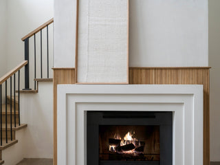 Custom concrete fireplace surround in white concrete with stepped rectangles against a reeded wall in a light wood tone.