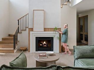 Wide view of a spacious living room with stepped white concrete fireplace surround, netural color palette with sage green sofa and accents.