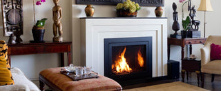Traditional living room with a contemporary black-framed gas fireplace insert set in a crisp white concrete surround, styled with eclectic wood furnishings, sculptural decor, and vibrant orchids—perfect for transitional interiors and upscale remodels